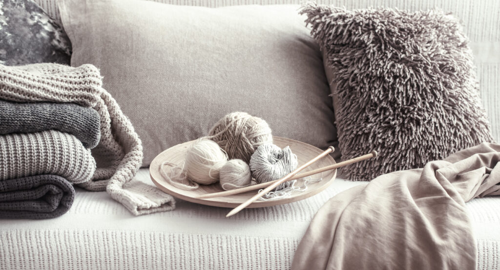 Vintage wooden knitting needles and threads for knitting on a cozy sofa with pillows and sweaters